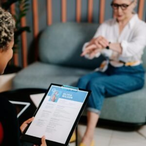 A senior woman being interviewed indoors with her resume displayed.